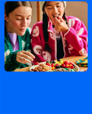 two girls having snacks of fruit, cookies and granola minis - mobile version